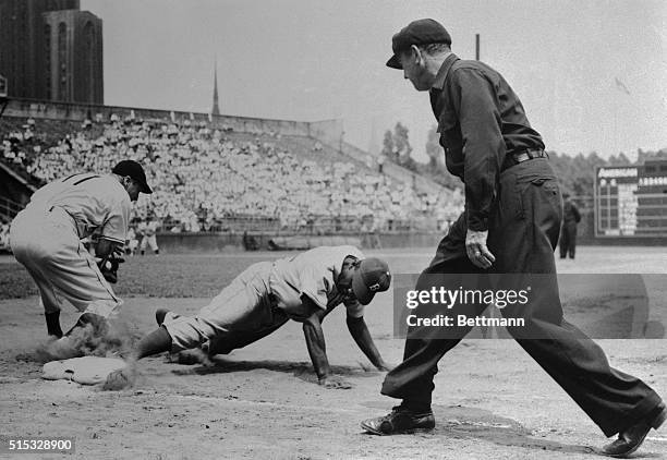 Jackie Robinson of the Dodgers slides back to first after he almost got picked off by Pirates in the second inning of the game with the Pirates, at...
