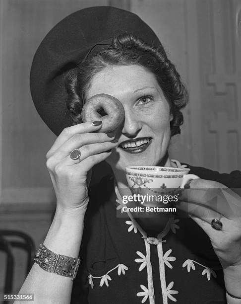 Baroness Irmeia Von Koschembaur, refugee from Saxony, Germany, is shown using a doughnut for a monocle during selection of "Doughnut-Drinking...
