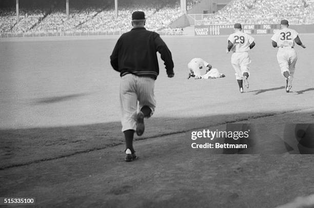 Fifth inning casualty, right-fielder Mickey Mantle, lies in a heap on the sod as Joe DiMaggio bends over him when Mantle collapsed with an injured...