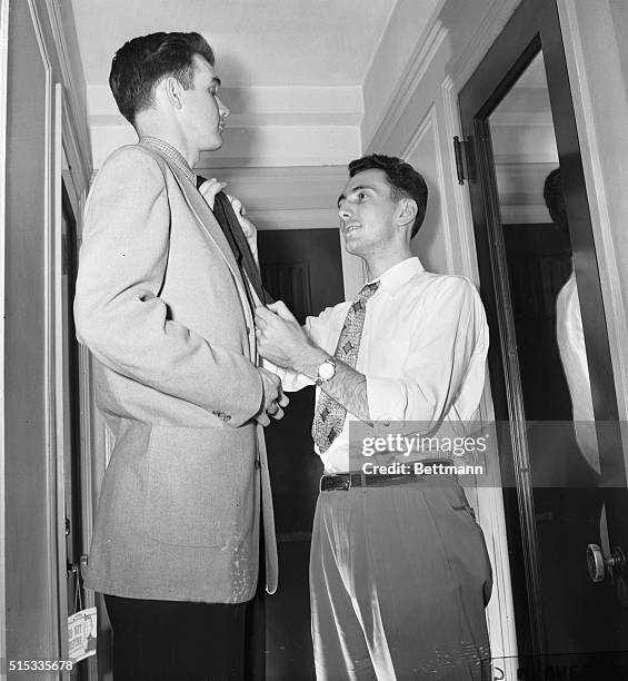 Bob Cousy , star basketball player with with the Boston Celtics, looks too short for pro basketball as he reaches to straighten the tie of teammate...