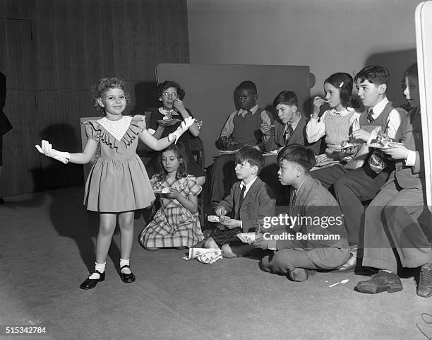 Children of United Nations personnel enjoy their ice cream as Robin Morgan models a dress designed to be worn when a child sits for her first...