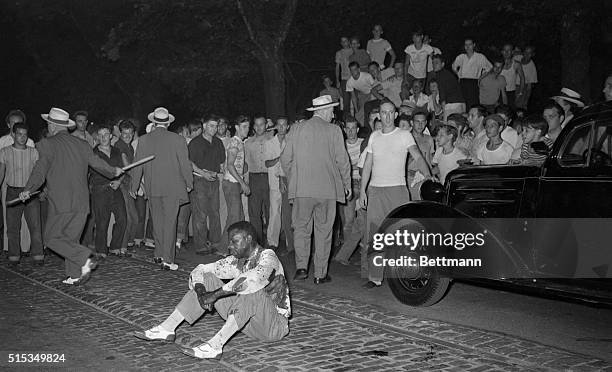 Beaten and bloody, a negro sits in the middle of the street while police check members of the mob which attacked and stoned him during a racie riot,...