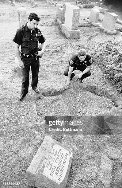 The defiled grave of movie producer Mike Todd is checked by policemen Richard Bisluk and Robert Kutak after it was discovered that Todd's coffin was...