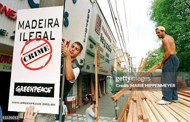 Greenpeace activist hangs a sign in Sao Paulo 15 December calling attention to the illegal wood being cut in the Amazon, while a worker unloads wood...