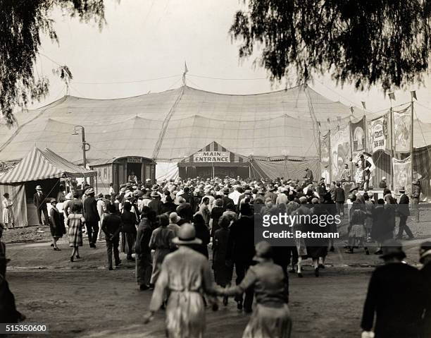 Photo shows a crowd of people at the entrance to a circus tent. On the right, sideshow attractions can be seen. Ca. Late 1920s-early 1903s.