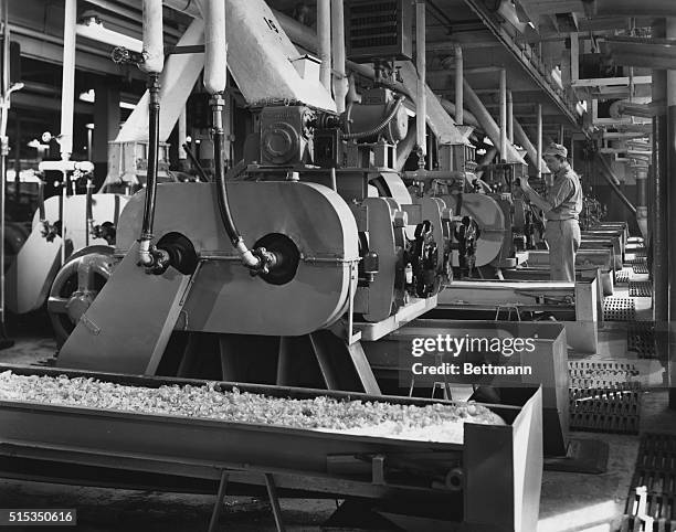 Interior view of a cereal manufacturing plant. Shows a man adjusting the tension of the machine rollers, in the flaking mill section of the Corn...