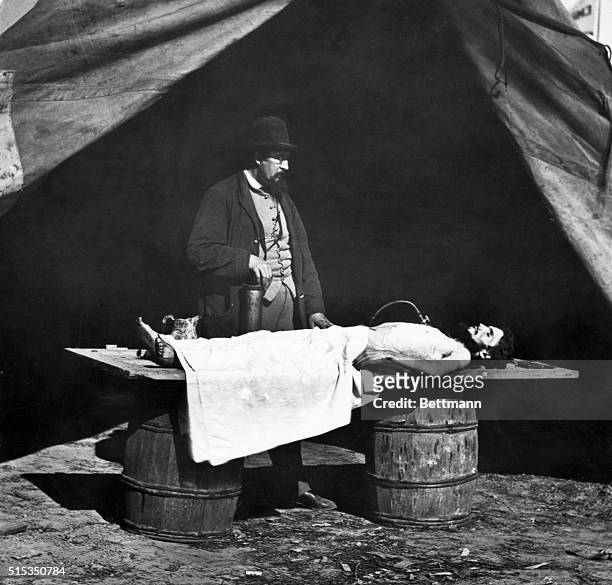 Embalming surgeon at work on a Civil War soldier's body. The corpse is lying outside a tent, on a door supported by two barrels. Undated photograph.
