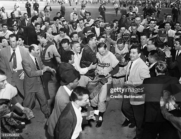 New York, NY: Young southpaw Johnny Podres folowed by masked Dodger Catcher Roy Campanella is literally mobbed by admiring fans who poured onto the...
