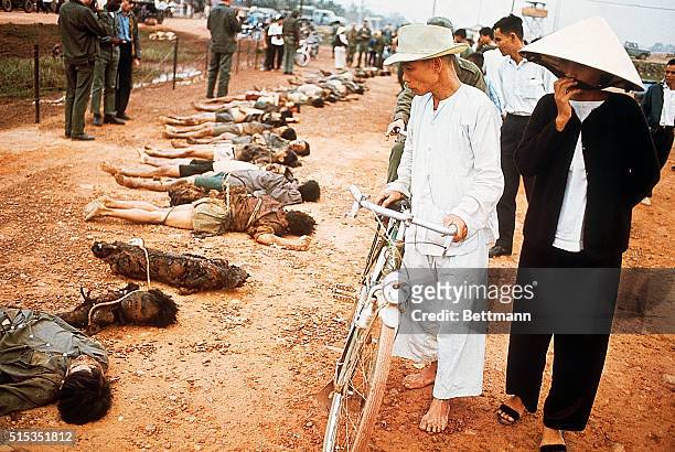 Group of Vietnamese walk past a row of corpses, victims of the Vietnam War.