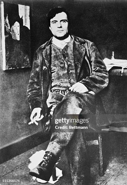 Italian painter Amadeo Modigliani relaxing in his studio. One of his trademark paintings of a woman's face hangs on the wall behind him.