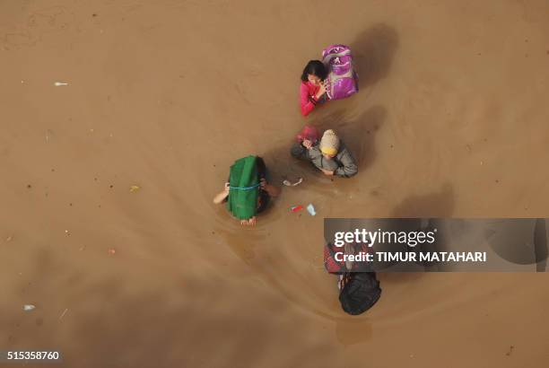 Residents wade through a flooded street in Bandung, West Java on March 13, 2016. - Thousands of people fled their homes as the Citarum river...