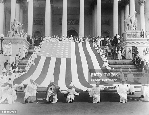 Ku Klux Klansmen draping giant American flag over Capitol steps.