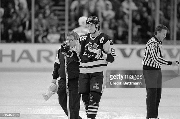 Pittsburgh Penguins Captain Mario Lemieux is escorted off the ice by trainer S. Thayer, after taking a slash on the wrist from the New York Ranger's...
