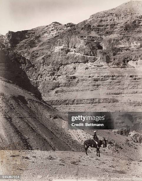 Palestinian man rides a donkey through a mountainous region.