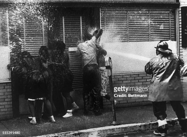Firemen bear in on a group of African Americans who sought shelter in a doorway as hoses and dogs were used in routing anti-segregation demonstrators...