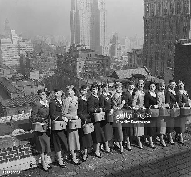 Thirteen of the twenty-one air stewardesses who are competing for the "Miss Skyway" Award pose on the Biltmore Hotel roof against the familiar New...