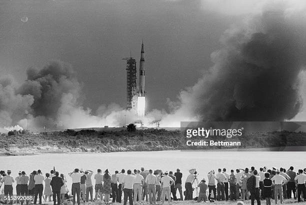The Apollo 11 mission gets underway at 9:32 A.M. EDT, as the Saturn V rocket, carrying the spacecraft on its nose, blasts off. Photo shows a small...
