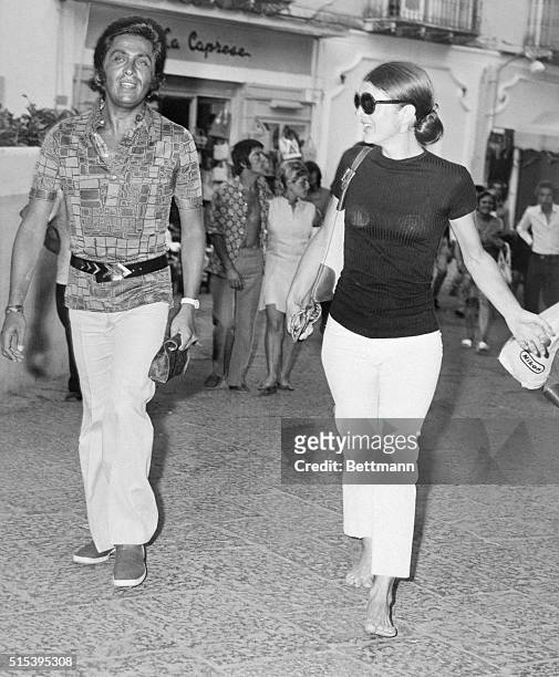 Mrs. Jacqueline Onassis walks barefooted with the king of Italian fashion, Valentino, during a sightseeing tour of this tiny island. Townspeople...