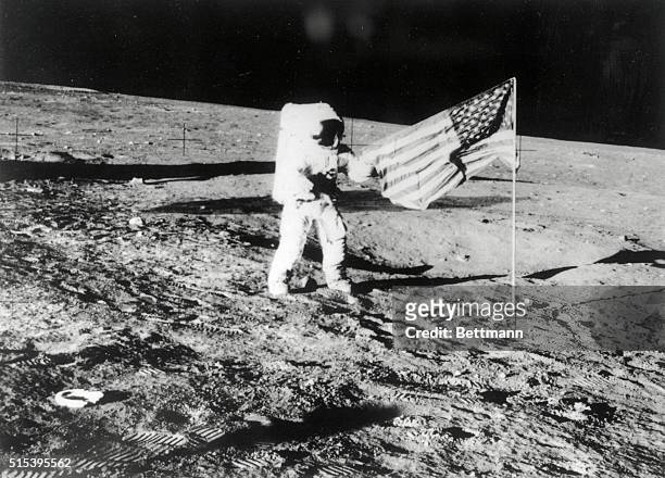 One of the Apollo 12 astronauts reaches out to extend the American Flag they erected on the lunar surface after their successful pin-point landing....