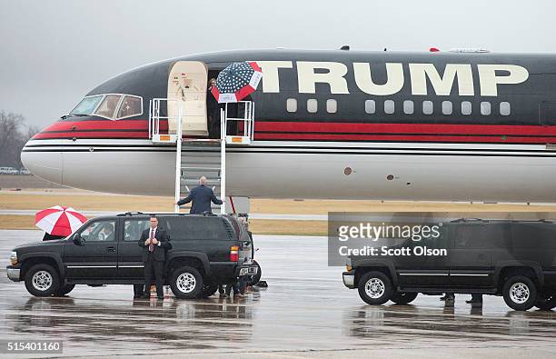 Under a red-white-and-blue umbrella Republican presidential candidate Donald Trump leaves a rally at the Central Illinois Regional Airport on March...