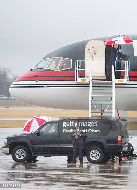 Under a red-white-and-blue umbrella Republican presidential candidate Donald Trump leaves a rally at the Central Illinois Regional Airport on March...