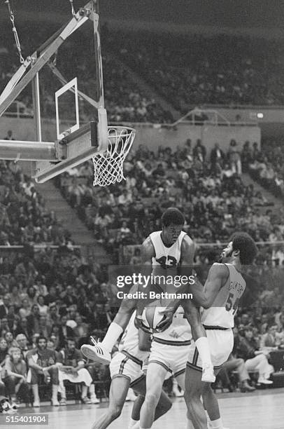 Uniondale, N.Y.: ABA's Ralph Simpson of the Denver Rockets, leaps high to grab rebound during game. At right is teammate Artis Gilmore. NBA defeated...