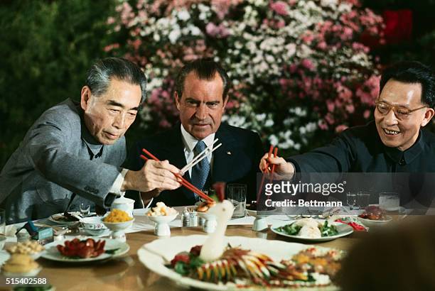 President Nixon holds his chopsticks in the ready position as Premier Chou En-lai and Shanghai Communist Party leader Chang Chun-chiao reach in front...