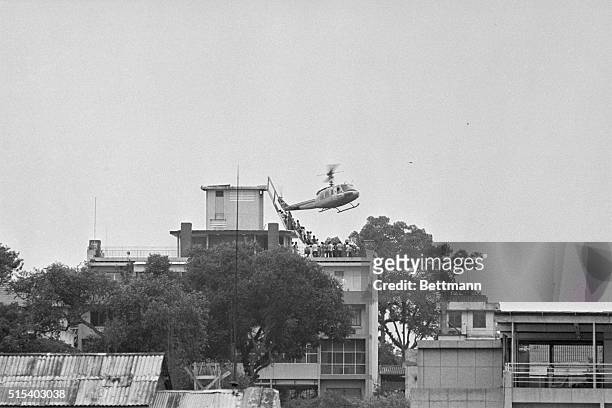 Saigon, South Vietnam: Air America helicopter crewman helps evacuees up the ladder on top of an apartment building. The evacuation side is one of...