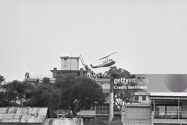 Air America helicopter crewman helps evacuees up the ladder on top of a Saigon building. The evacuation side is one of many in the downtown area from...