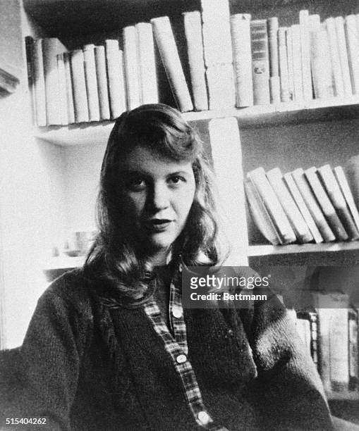 Photo shows author Sylvia Plath seated in front of a bookshelf.