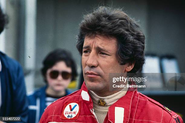 Close-up shows Mario Andretti, auto racer, in the pit area.