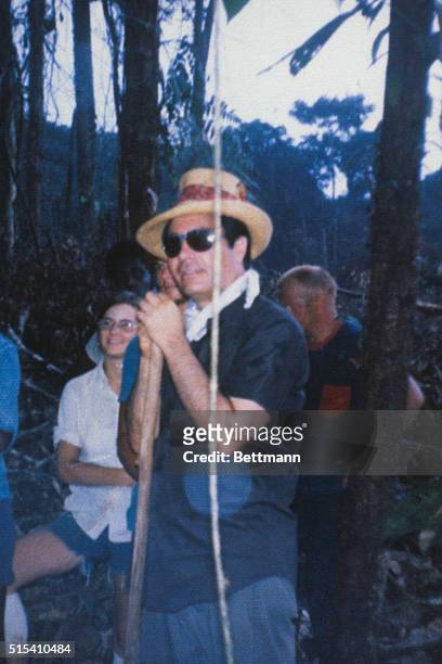 Jim Jones is shown wearing a straw hat and leaning on a stick while clearing area for his visionary "Jonestown."