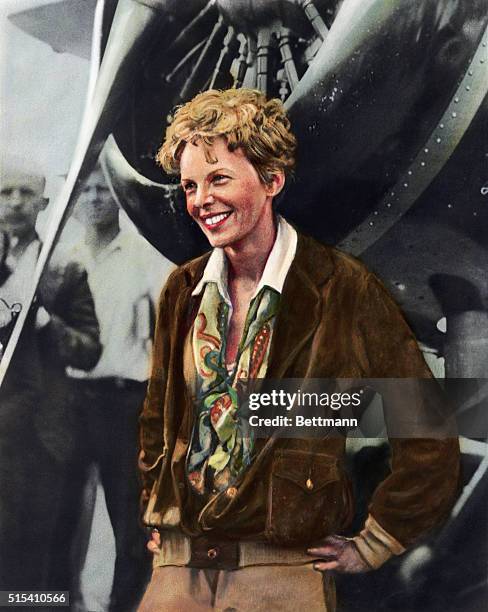 Hand-colored portrait of Amelia Earhart, , American aviator, smiling as she stands in front of her plane. Undated illustration.