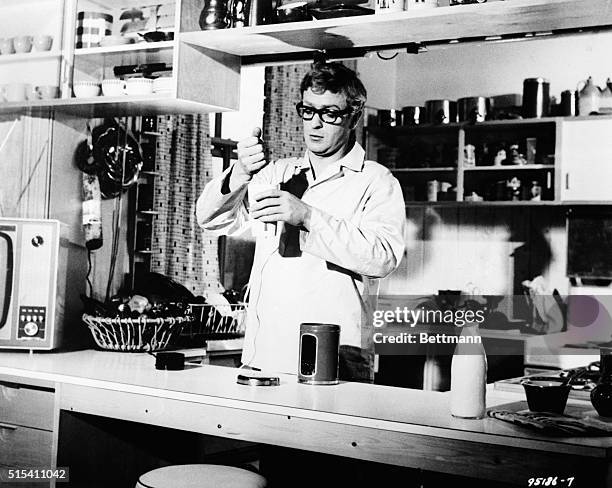 London, England-: Tumbling out of bed, Michael Caine goes straight to his kitchen and prepares coffee. "The Ipcress File," suspense drama of...
