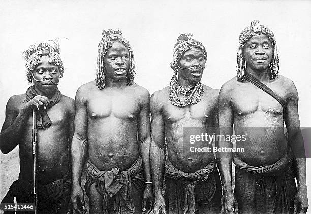 Four Tang men from the French Congo stand side-by-side. They wear only loincloths and their chests and stomachs bear ceremonial scars. Ca. 1900.