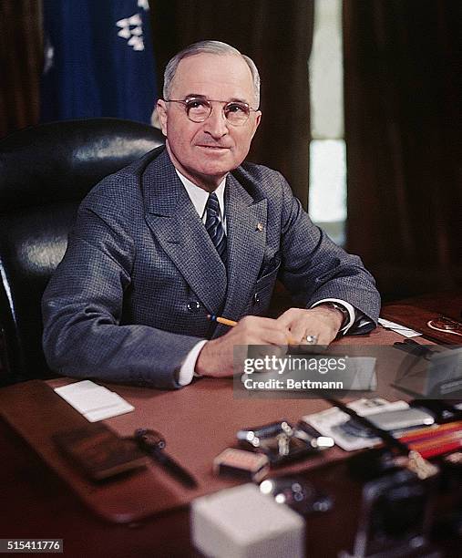 President Harry S. Truman seated at his desk holding a pencil.