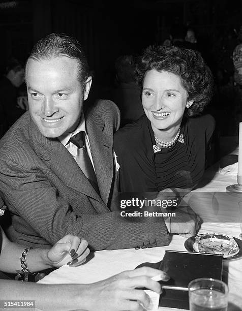 Comedian Bob Hope and his wife smile over at a friend during a dinner banquet.