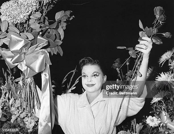 New York, NY-Still wearing the make-up from her clown role, songstress Judy Garland is surrounded by floral tributes to her talents which acclaimed...