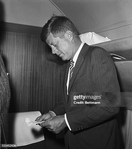President-elect John F. Kennedy, aboard an aircraft, reads radio messages informing him that his wife had been rushed to a Washington hospital for...