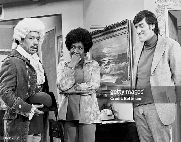 Isabel Sanford, as Louise, inspects an oddly dressed Sherman Hemsley , as George, while Paul Benedict, as Harry Bentley, looks on, in the...