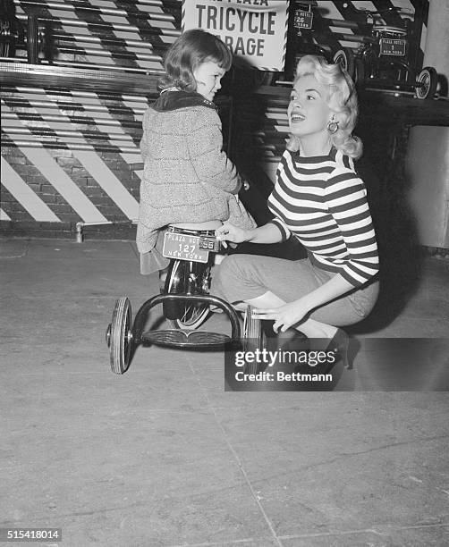 Actress Jayne Mansfield adjusts the new 1956 license plate on the three wheeler of her 5 year old daughter, Jayne Marie, at a local tricycle garage....