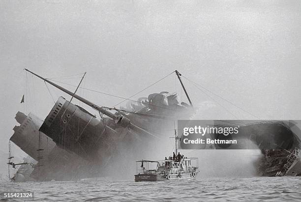 Death of a Queen,. Hong Kong: Fireboat plays water on the still-burning blackened hull of the former Queen Elizabeth here, after she rolled over...