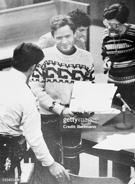 Tallahassee, Fla.: Suspected mass killer Theodore R. Bundy, with legal files in hand and a puzzling smile on his face, is escorted from the Leon...