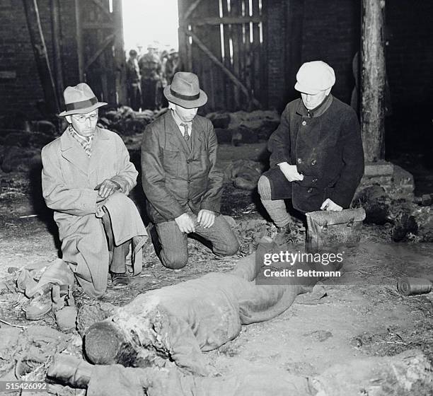 Three German burgomeisters grimly view the charred body of a victim of mass execution by Nazi at Gardelegen. American soldiers in background look in...