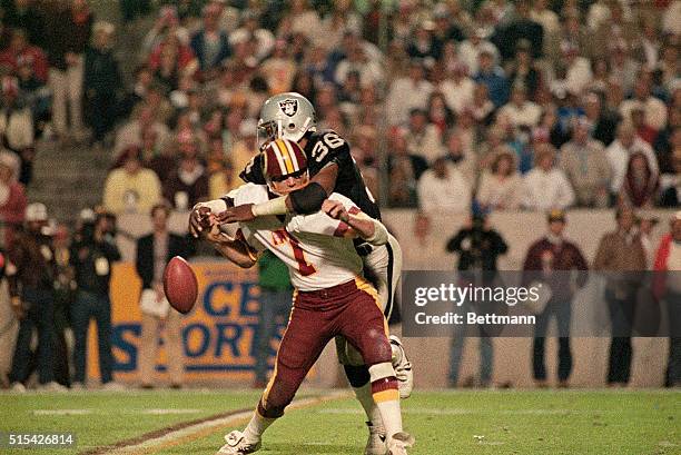 Joe Theismann of the Washington Redskins tackled by a member of the Oakland Raiders during Super Bowl game.