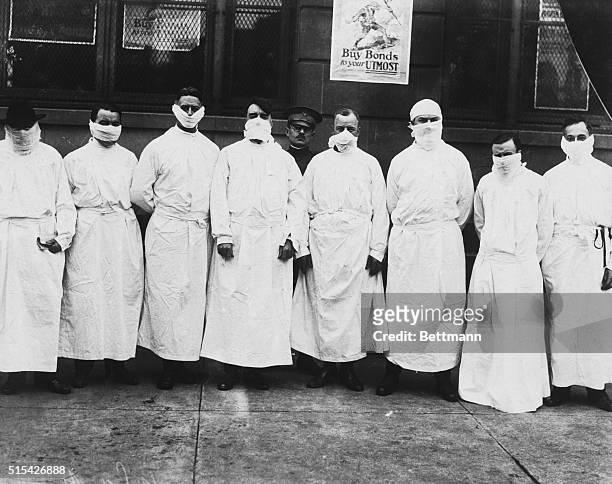 Doctors, army officers, and reporters wear surgical gowns and masks while making a tour of a hospital to observe Spanish influenza treatment of...