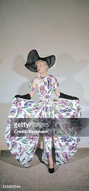 The fashion of 1950 is shown in a Paquin creation for summer evening wear. It is of white linen, with green and purple flowers printed on. The high...