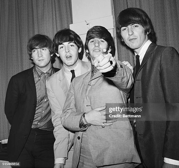 Ringo Starr points at the camera as fellow Beatles John Lennon, Paul McCartney, and George Harrison stand beside him backstage at a charity...