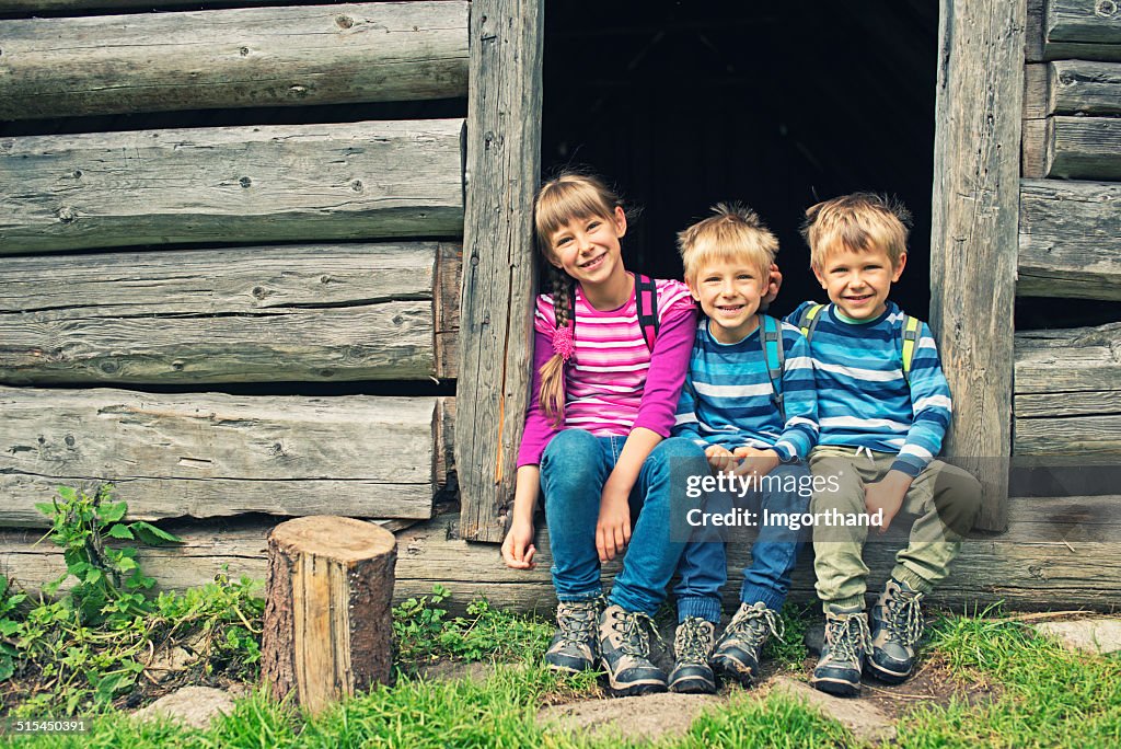 Little hikers resting in front of old wood cabin