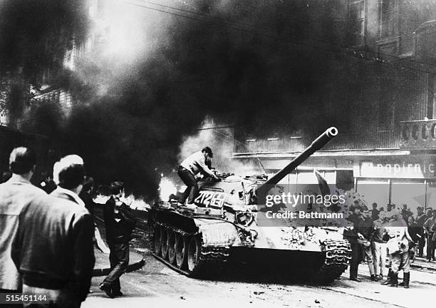 Prague, Czechoslovakia- Black smoke fills the street as a Czech youth climbs aboard a Russian tank during demonstration near the Prague radio station...